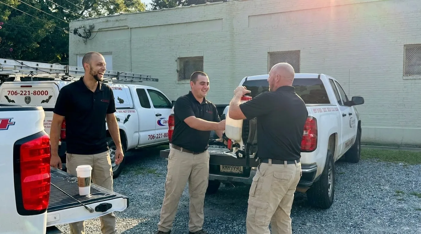 Three Jarrod's technicians laughing as they load a sprayer into a truck in the morning