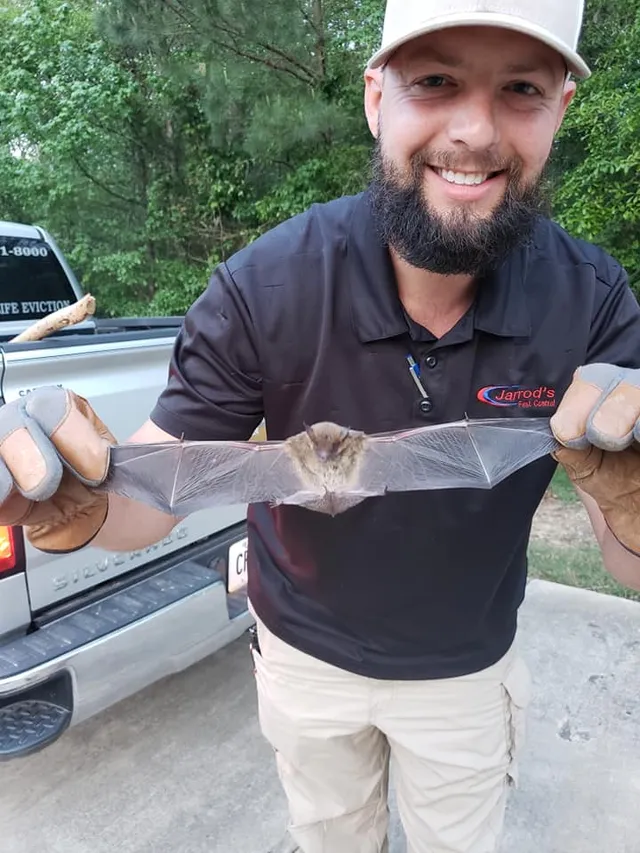 A smiling Jarrod's technician in a company polo holding a bat he removed
